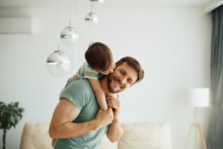 Little boy kissing his father who is piggybacking him while spending time together at home.