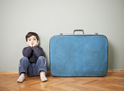 child sitting next to a suitcase
