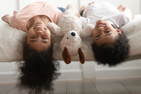 Funny cute little boy and girl laughing lying upside down on bed with toy.