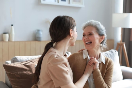Happy senior mom and adult daughter embracing with love on sofa